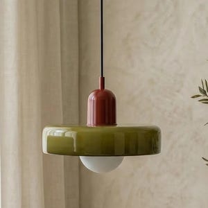 May include: A modern pendant light with a red top, olive green shade, and a white globe-shaped light. The light hangs from a black cord, creating a stylish and contemporary lighting fixture. The design is minimalist and suitable for various interior styles.