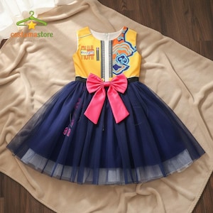 Może przedstawiać: Bezrękawnik żółto-granatowa sukienka z różową kokardą. Gorset ma kolorowy wzór i napis "ATTENTION". Spódnica jest warstwowa z granatowego tiulu. Sukienka jest przeznaczona dla dzieci.