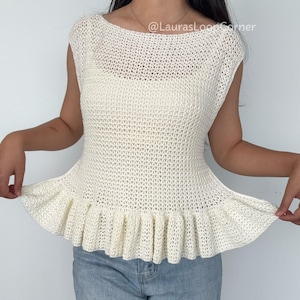 Peut inclure: Un haut sans manches en crochet de couleur crème avec une large encolure bateau et un ourlet à basque évasé. Le vêtement présente une texture en maille ajourée et le texte @LaurasLoopCorner est imprimé en blanc sur la poitrine.