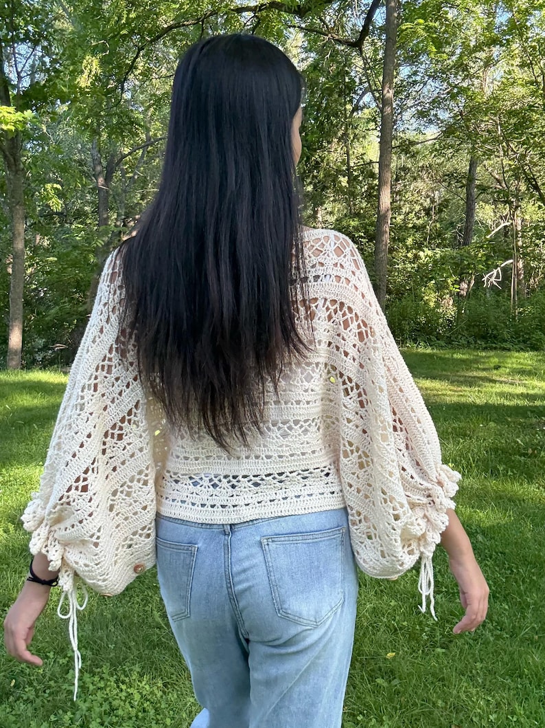 Pu&ograve; includere: Un top all'uncinetto color crema caratterizzato da lunghe e voluminose maniche a vescovo con lacci ai polsini e un complesso motivo traforato su tutto il corpetto e le maniche, abbinato a jeans in denim azzurro.
