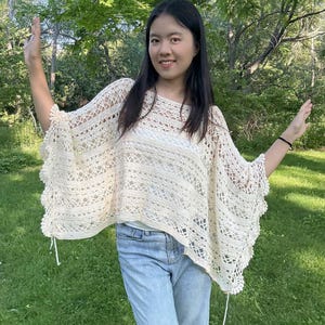 Pu&ograve; includere: Un poncho all'uncinetto color bianco sporco caratterizzato da un intricato motivo traforato con fasce orizzontali a maglia piena e un bordo smerlato. Il capo presenta una vestibilit&agrave; ampia con scollo a barchetta e delicati laccetti laterali.