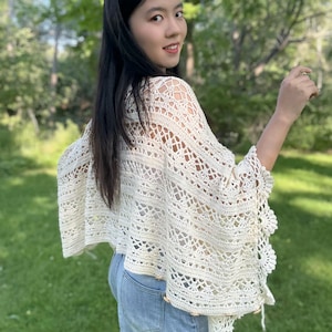 Pu&ograve; includere: Un poncho all'uncinetto color bianco sporco caratterizzato da un intricato motivo traforato con disegni geometrici e floreali. Il capo presenta un bordo smerlato lungo l'orlo ed &egrave; arricchito da piccoli bottoni rotondi in legno sul lato.