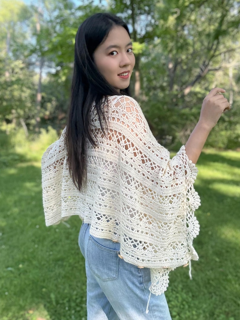 Pu&ograve; includere: Un poncho all'uncinetto color bianco sporco caratterizzato da un intricato motivo traforato con disegni geometrici e floreali. Il capo presenta un bordo smerlato lungo l'orlo ed &egrave; arricchito da piccoli bottoni rotondi in legno sul lato.