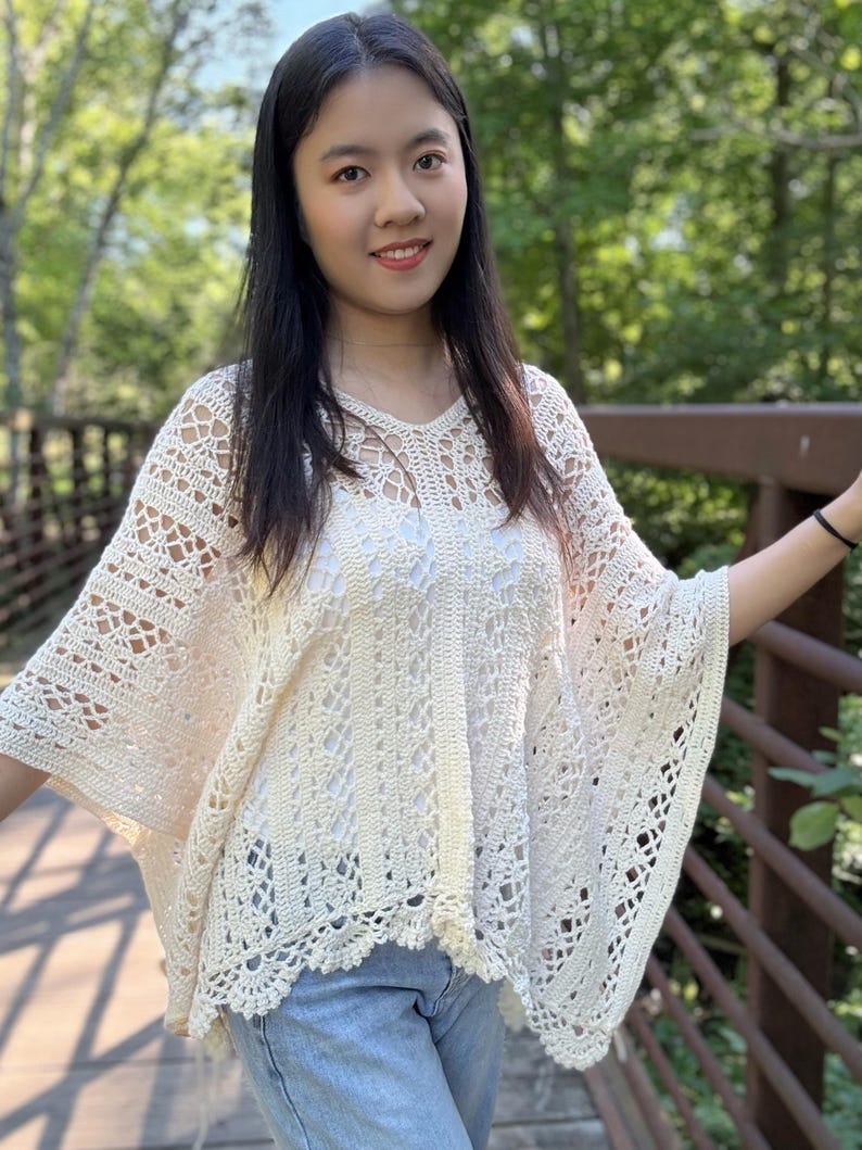 Pu&ograve; includere: Un poncho all'uncinetto color crema caratterizzato da un intricato motivo in pizzo traforato con scollo a V e orlo smerlato. Il capo &egrave; indossato sopra un top bianco e jeans azzurri, mostrando una silhouette ampia e fluida con maniche larghe.