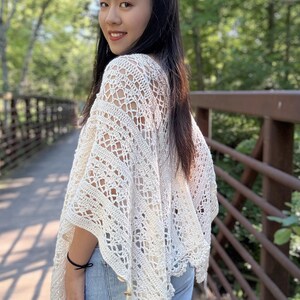 Pu&ograve; includere: Un poncho all'uncinetto color bianco sporco caratterizzato da un intricato motivo traforato con disegni geometrici e floreali. Il capo presenta una silhouette ampia e drappeggiata con orli a punta e piccoli bottoni in legno sui lati.