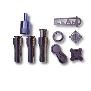 May include: An assortment of dark gray metal machine parts, including cylindrical pieces, a ring, and a component with the word "LEAN" cut out. One part has the number "25" etched on it. The parts are arranged on a white background.