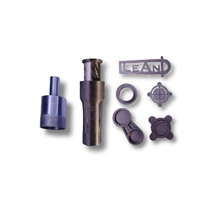 May include: An assortment of dark gray metal machine parts, including a cylindrical piece with the number "25" etched on it, a long tube, and several smaller components. One piece has the word "LEAN" cut out.