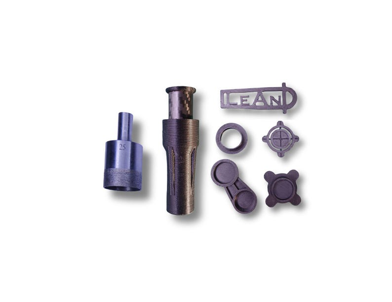 May include: An assortment of dark gray metal machine parts, including a cylindrical piece with the number "25" etched on it, a long tube, and several smaller components. One piece has the word "LEAN" cut out.