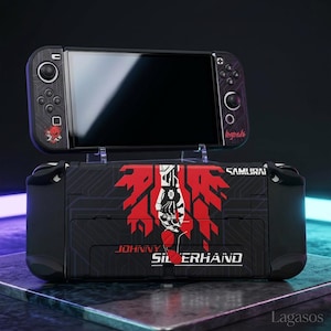 May include: Black and red custom Nintendo Switch console with a matching dock. The console features a design with the words "Johnny Silverhand" and "Samurai" in red and white. The console is resting on a clear stand.