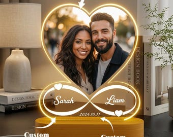 May include: A personalized LED night light with a heart-shaped frame holding a couple's photo. The base is wooden, with the names "Sarah" and "Liam" and the date "2024.10.11" displayed. The light has a warm glow.