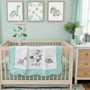 May include: A nursery with a light green color scheme features a wooden crib with a dinosaur-themed quilt and mobile. Three framed dinosaur art prints hang above the crib. A matching rug and dresser complete the room's decor.