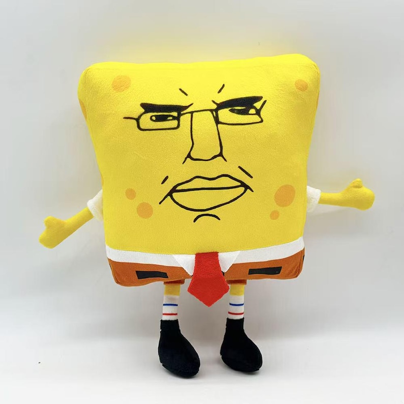 May include: A yellow plush toy resembling a cartoon character with a stern expression. The toy has a square body, a white shirt, a red tie, and brown shorts. It has black shoes and striped socks. The character's face features glasses and a frowning mouth.