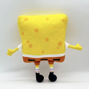 May include: A plush toy shaped like the cartoon character SpongeBob SquarePants. The toy is yellow with orange spots, brown shorts, white shirt sleeves, and black shoes. Arms and legs are extended.