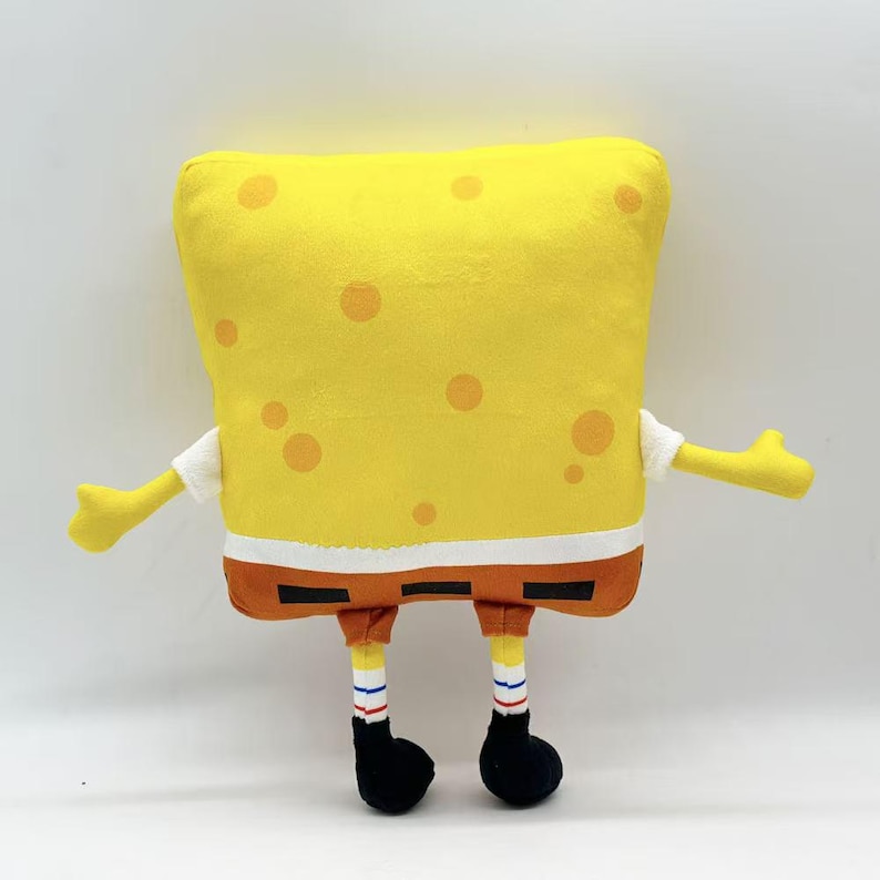 May include: A plush toy shaped like the cartoon character SpongeBob SquarePants. The toy is yellow with orange spots, brown shorts, white shirt sleeves, and black shoes. Arms and legs are extended.