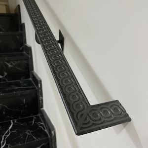 Könnte beinhalten: Dunkelgraues Metallgeländer mit sich wiederholendem kreisförmigem Muster. Das Geländer ist an einer weißen Wand befestigt und befindet sich über einer schwarzen Marmortreppe. Das Geländer wird von schwarzen Metallhalterungen getragen.