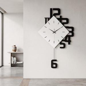 May include: A wall clock featuring a white diamond-shaped face with black hour markers and hands. Behind the face, large black numbers are arranged in a layered pattern. A thin black pendulum hangs below the clock, ending in a black number six.