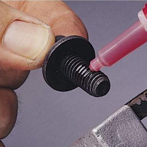 以下が含まれることがあります： 黒いボルトに、絞り出しボトルから赤い液体を塗布しているクローズアップ。ボルトは幅広で平らな頭部とねじ山のあるシャフトを持っています。赤い液体はねじ山に塗布されています。