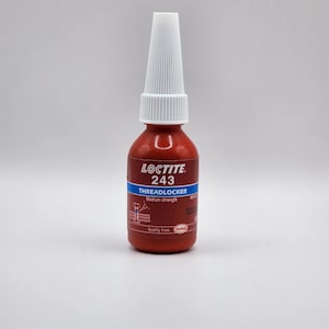 May include: A red Loctite 243 Threadlocker bottle with a white nozzle. The label features the product name, strength, and a diagram. The bottle is designed for medium-strength thread locking applications.