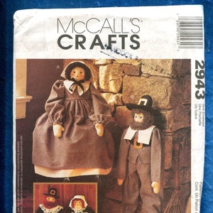 May include: A vintage sewing pattern for making four pilgrim dolls. The pattern is from McCall's Crafts and is numbered 2943. The dolls are dressed in brown and white clothing and have black hats. The pattern includes instructions for making the dolls and their clothing.