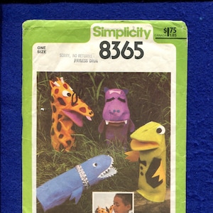 May include: Simplicity pattern 8365 featuring hand puppets: a giraffe, hippo, shark, and frog. The giraffe is orange and yellow, the hippo is purple, the shark is blue, and the frog is green and yellow. The pattern includes the text "Sorry, No Returns".