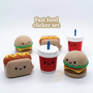 Può includere: Un set di clicker a tema fast food, tra cui un hamburger, un hot dog e un bicchiere di soda, ognuno con una faccia sorridente. Il set include il testo "Fast food clicker set". I clicker sono in tonalità di marrone, rosso, giallo e verde.