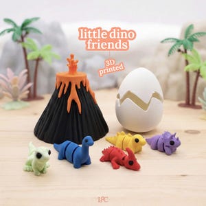 Può includere: Una collezione di giocattoli e accessori di dinosauri stampati in 3D. Include un vulcano nero con lava arancione, un uovo bianco e figure di dinosauri colorate in verde, blu, rosso, giallo e viola. Il testo "little dino friends" e "3D printed" sono visibili.