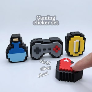 May include: A gaming clicker set with pixelated designs. Includes a blue potion, a grey controller, a yellow coin, and a red button. The text "Gaming clicker set" is visible.