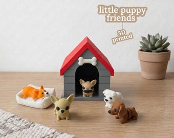 May include: A collection of 3D-printed puppy figurines, including a corgi, chihuahua, and dachshund, with a doghouse and a small succulent plant. The doghouse is gray with a red roof and a bone-shaped detail. The text "little puppy friends" is visible.