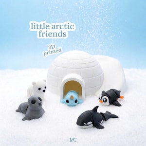 May include: A 3D-printed diorama featuring an igloo and several arctic animal figurines. The figurines include a polar bear, seal, narwhal, penguin, and orca. The text "little arctic friends" and "3D printed" are displayed on a light blue background.