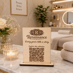 Peut inclure: Un panneau rectangulaire en bois clair avec un logo gravé foncé présentant la lettre R, le mot Renaissance, la phrase Every grain tells a story, le texte Explore the collection et un code QR carré sur un socle en bois assorti.
