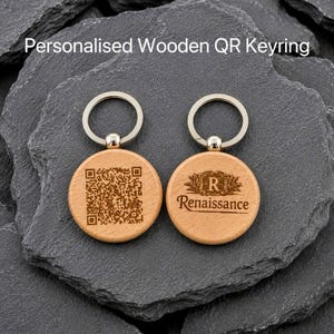 May include: Two round light brown wooden keyrings with silver metal rings. One keyring features a laser-engraved QR code, while the other displays a decorative crest with the letter R and the text Renaissance engraved in the centre.