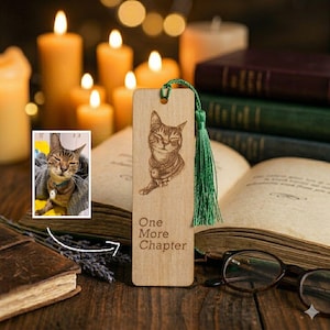 Può includere: Segnalibro in legno con illustrazione di gatto incisa al laser e la scritta "One More Chapter". Il segnalibro ha un nappa verde ed è ambientato su uno sfondo di libri e candele. È inclusa anche una piccola foto di un gatto.