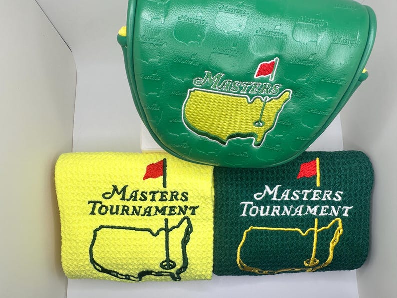 Puede incluir: Funda verde para la cabeza del palo de golf y dos toallas de golf. La funda tiene la palabra "Masters" y un mapa del campo de golf bordado. Las toallas son amarillas y verdes, con las palabras "Masters Tournament" y un mapa del campo.