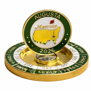 Peut inclure: Un marqueur de balle de golf doré avec une bordure verte et blanche, avec le mot "AUGUSTA" et "MASTERS". Le marqueur a une carte des États-Unis et l'année 2026. La base comporte des marquages de distance.