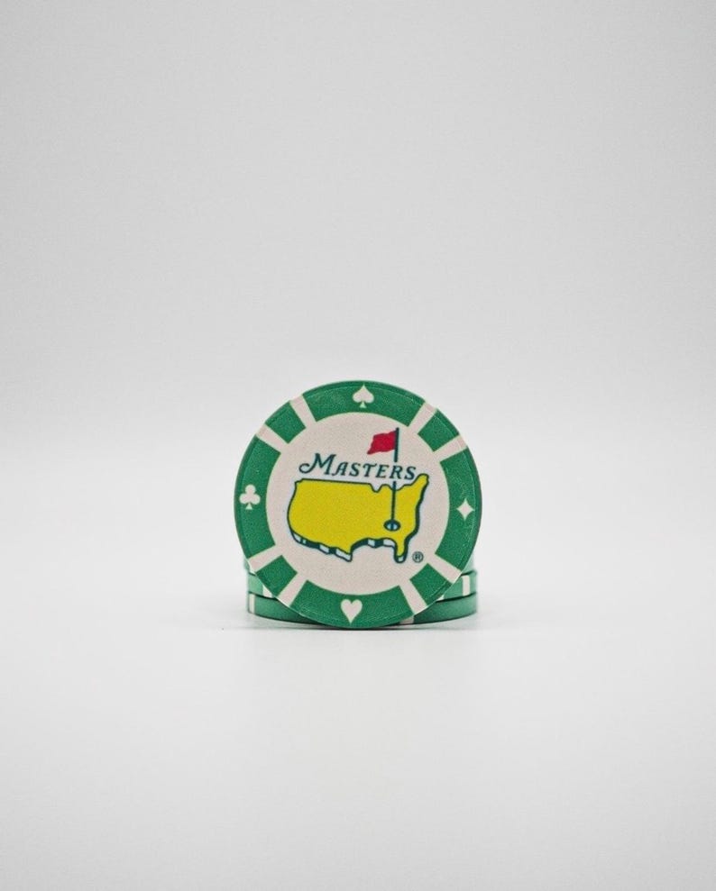 May include: A stack of green and white poker chips. Each chip features the Masters logo, a yellow outline of the United States with a red flag, and the word "Masters". The chips have suit symbols around the edge.