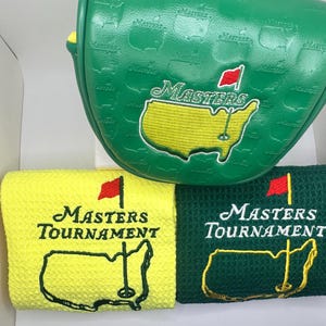 Puede incluir: Funda verde para la cabeza del palo de golf y dos toallas de golf. La funda tiene un mapa de los Estados Unidos con la palabra "Masters" y una bandera roja. Las toallas son amarillas y verdes, con las palabras "Masters Tournament" y un mapa de los Estados Unidos.