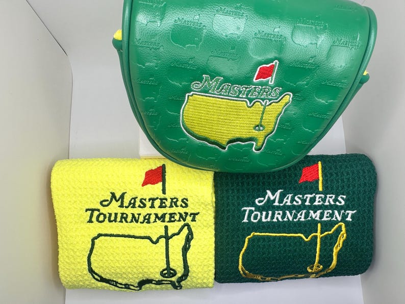 Puede incluir: Funda verde para la cabeza del palo de golf y dos toallas de golf. La funda tiene un mapa de los Estados Unidos con la palabra "Masters" y una bandera roja. Las toallas son amarillas y verdes, con las palabras "Masters Tournament" y un mapa de los Estados Unidos.