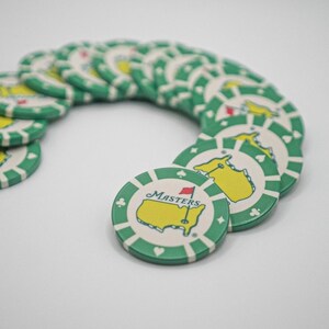 May include: A collection of green and white poker chips. Each chip features a yellow map with a red flag and the word "Masters". The chips have a green border with white stripes and suit symbols.