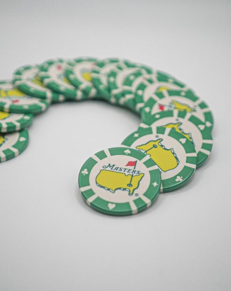 May include: A collection of green and white poker chips. Each chip features a yellow map with a red flag and the word "Masters". The chips have a green border with white stripes and suit symbols.