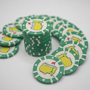 May include: A stack of green and white poker chips with the Masters logo. The chips feature a yellow outline of the state of Georgia with a red flag and the word "Masters". The chips are arranged in a semi-circle.