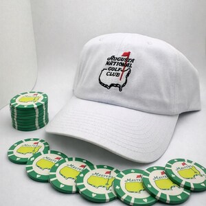 Può includere: Cappellino da baseball bianco con logo "Augusta National Golf Club" e una pila di fiches da poker da golf verdi e bianche. Le fiches presentano un disegno a mappa verde e la scritta "Masters".