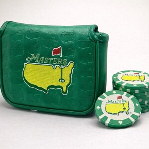 May include: Green golf putter cover and golf chips. The putter cover has the Masters logo in yellow and white. The golf chips are green and white with the Masters logo and a red flag.