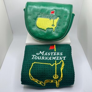 May include: A green golf club head cover and a matching green towel. Both items feature the Masters Tournament logo, including a yellow map of the United States with a red flag and the word "Masters" in white.