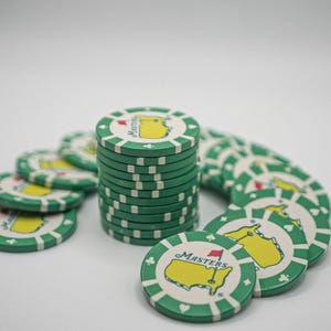 May include: A collection of green and white poker chips. Each chip features a yellow map design with a red flag and the word "Masters". The chips are stacked and scattered, suggesting a game or collection.