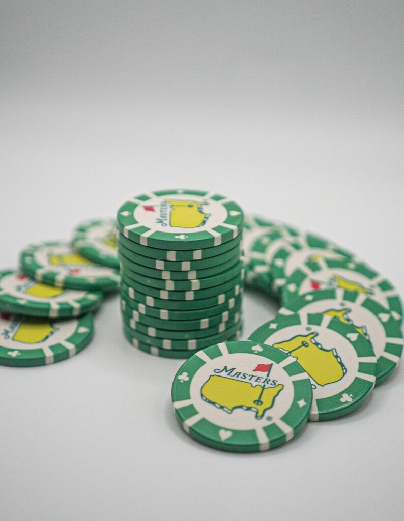 May include: A collection of green and white poker chips. Each chip features a yellow map design with a red flag and the word "Masters". The chips are stacked and scattered, suggesting a game or collection.