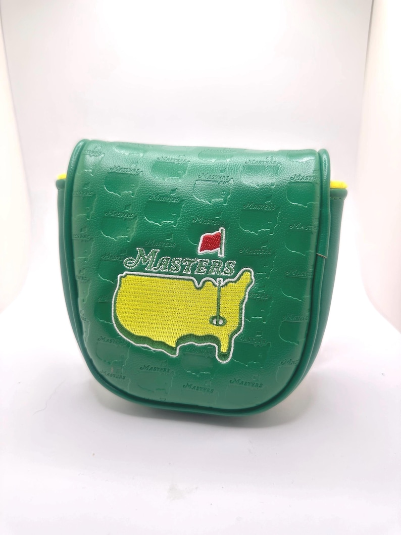 May include: Green golf putter cover with the Masters logo. The cover features a yellow and green map of the United States with a red flag and the word "Masters" in white. The cover is made of a textured material.