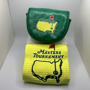 May include: Green golf club cover and yellow golf towel. The cover has the word "Masters" and a map of Georgia with a red flag. The towel has the words "Masters Tournament" and a map of Georgia with a golf pin.