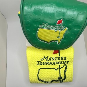 May include: Green golf club head cover and yellow golf towel. The head cover has the word "Masters" and a map of the course embroidered on it. The towel has the words "Masters Tournament" and a map of the course embroidered on it.