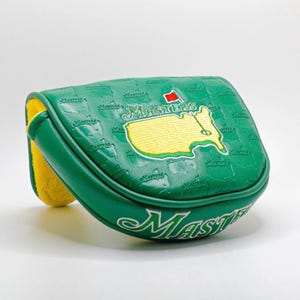 May include: Green golf putter cover with the word "Masters" in white script. The cover features a yellow embroidered map of the Augusta National Golf Club course and a red flag. The cover is green with a yellow interior.