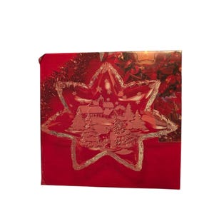 May include: A red Christmas-themed gift box with a star-shaped glass dish on top. The dish features an etched winter village scene with trees and houses. The box has a shiny, reflective surface.
